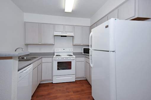 A white refrigerator stands in a kitchen with wooden floors and white cabinets.