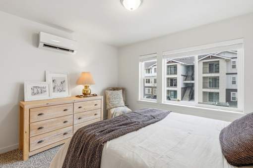 A bedroom with a large bed, a dresser, and a window overlooking a building.