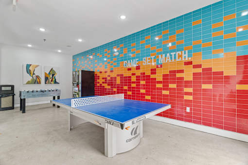 A ping pong table is in a room with a colorful wall.
