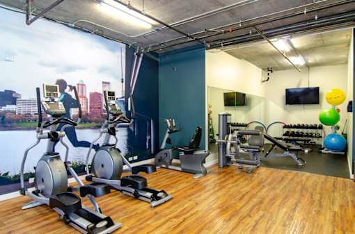 A gym with exercise equipment and a cityscape mural on the wall.