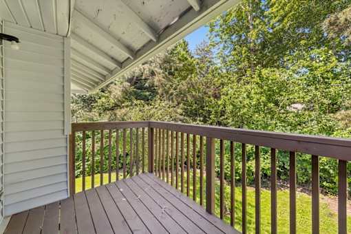 A wooden deck with a white house and trees in the background.