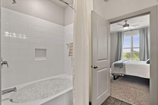 A white bathroom with a tub and a bedroom with a bed.