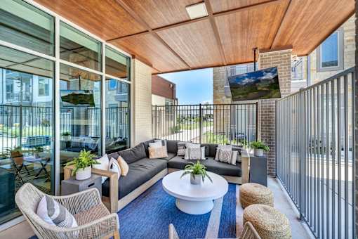 A modern balcony with a sofa, chairs, and a TV.