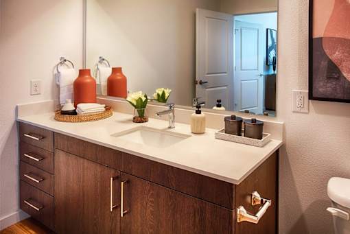 A bathroom with a white counter top and wooden cabinets.