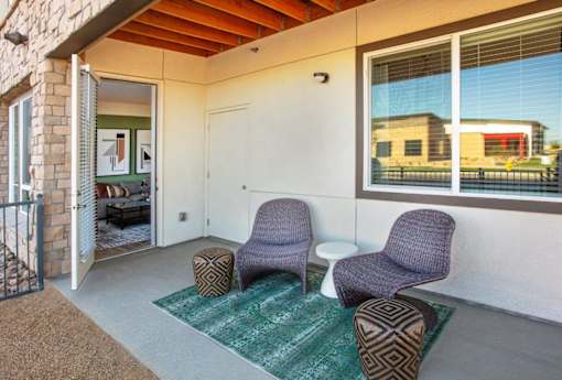 A patio with two chairs and ottoman with a green rug.