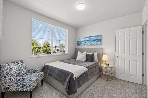 A bedroom with a bed, chair, and painting.
