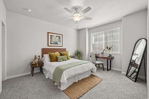A bedroom with a bed, desk, chair, and a ceiling fan.