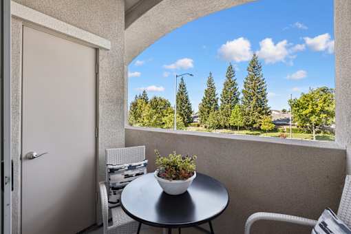 A balcony with a table and chairs overlooking a tree-filled landscape.