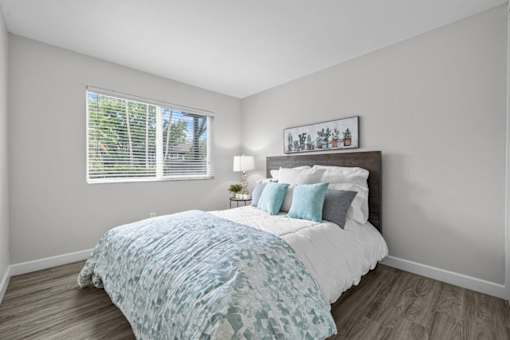 A bedroom with a bed, pillows, and a picture frame on the wall.