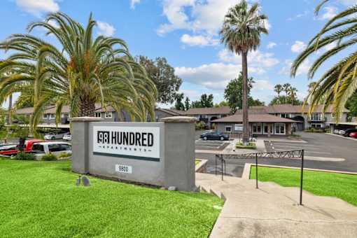 A concrete sign for Hundred Apartments is in front of a grassy area.