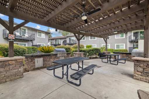 A patio with a table and benches under a roof.