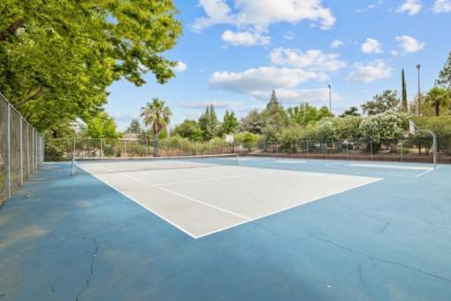 A tennis court surrounded by trees and a fence.