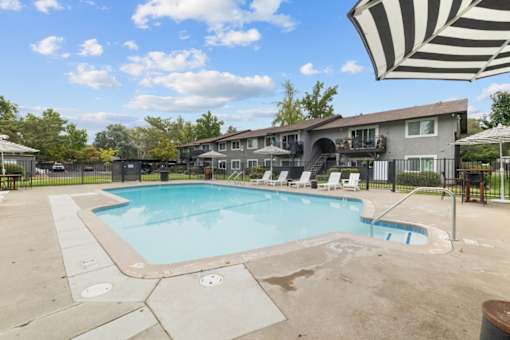 A large outdoor swimming pool surrounded by a concrete patio and a striped umbrella.