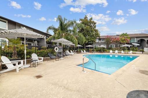 A pool area with chairs and umbrellas in front of a building.