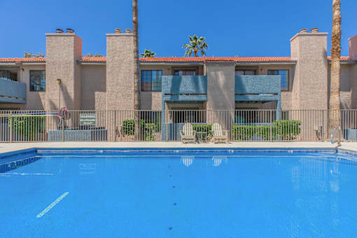 A swimming pool in front of a building with a palm tree.