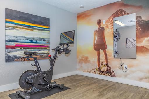 A room with a stationary bike in front of a wall with a painting of a woman on it.