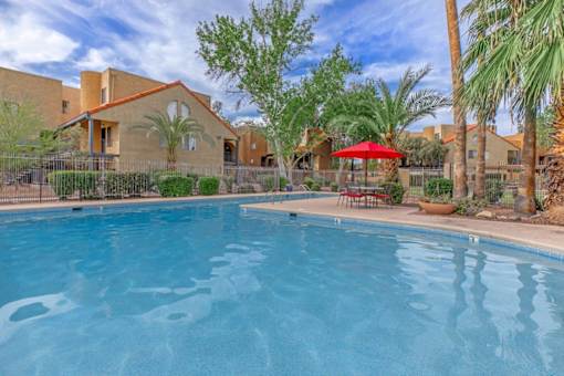 A swimming pool in front of a house with a red umbrella.