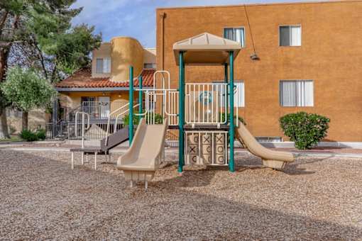 A playground with a slide and a swing set in front of a building.
