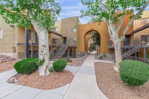 A courtyard with a pathway, trees, and bushes in front of apartment buildings.