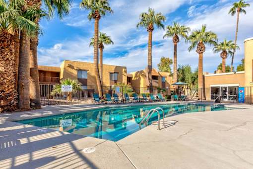 A pool surrounded by palm trees and a building in the background.
