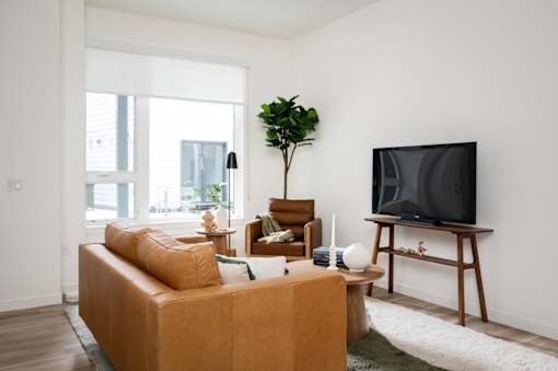 The Wes Gresham Oregon Apartments A living room with a brown sofa, a wooden coffee table, a television, and a potted plant.