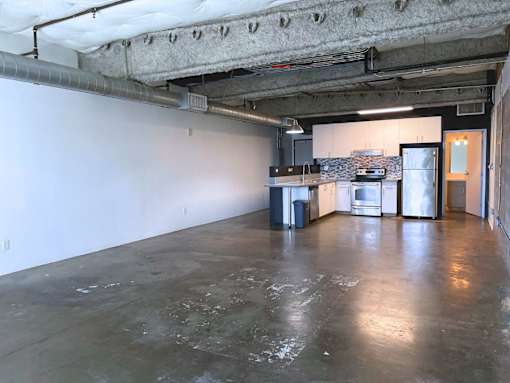 A large empty room with a kitchen area in the background.