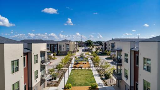 A view of a courtyard surrounded by buildings with a blue sky and clouds in the background.