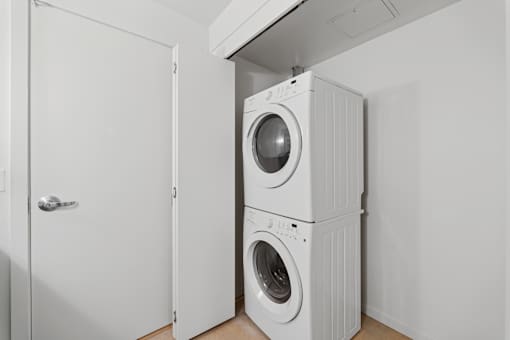 A white washing machine is stacked on top of another white washing machine in a small room.