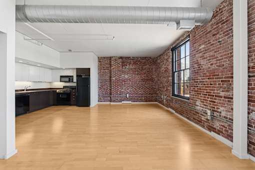 A large empty room with wooden floors and a brick wall.