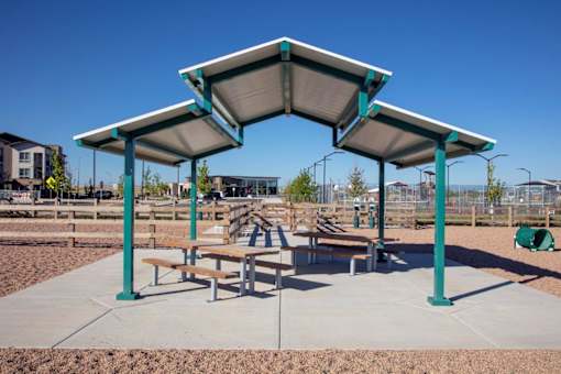 A playground with a shelter and benches is set in a sandy area.
