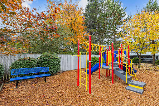 A playground with a red and yellow swing set and a blue bench.