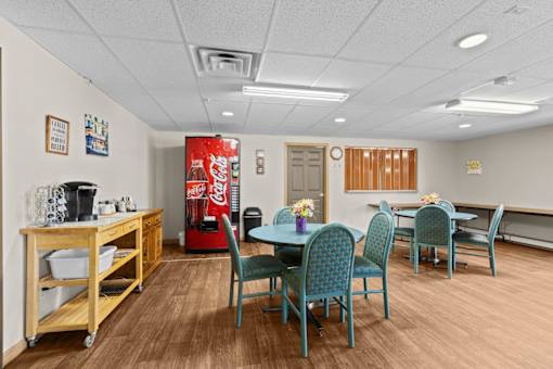 A room with a Coca-Cola machine and a dining table with chairs.