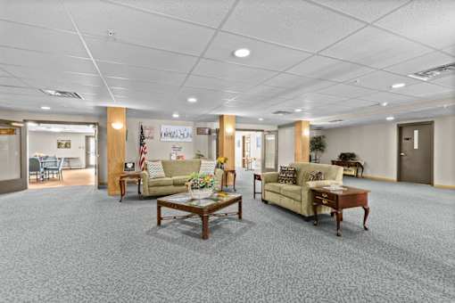 A spacious room with grey carpeting and furniture including a sofa, armchair, and coffee table.