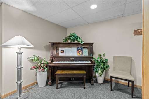 A room with a piano, a chair, and a floor lamp.