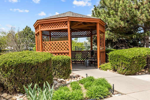 A wooden gazebo is surrounded by green plants and trees.