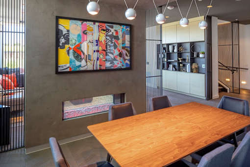 A large wooden table is surrounded by chairs in a room with a large painting on the wall.