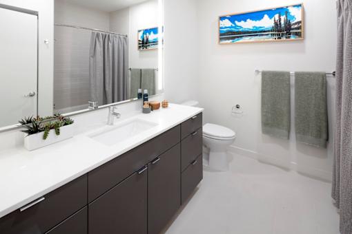 A bathroom with a white countertop and a painting of a beach scene on the wall.