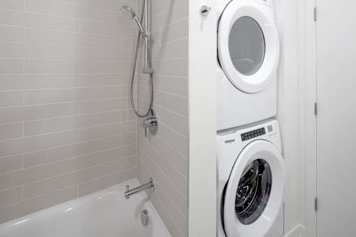 A white washing machine is in a bathroom next to a bathtub.