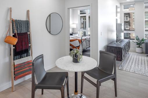 A white table with two chairs and a vase of flowers sits in a room with a mirror and a coat rack.