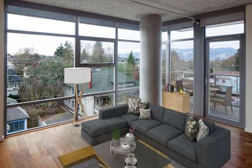 A grey couch with a glass table in front of a large window.