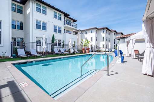 A swimming pool in front of a white apartment building.