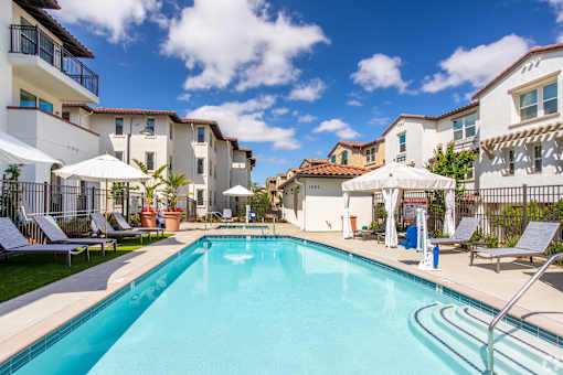 A swimming pool surrounded by lounge chairs and umbrellas in a sunny day.