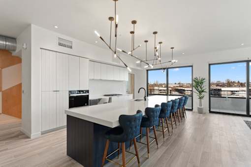 A modern kitchen with a long white island and blue chairs.