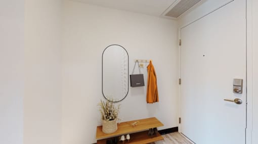 A white wall with a mirror, a bench, and a plant on it.