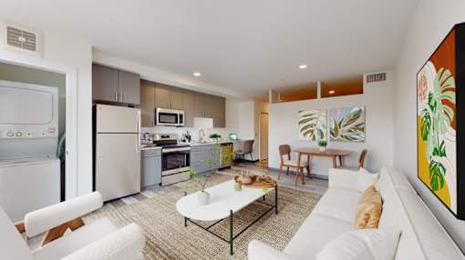 A modern kitchen with white appliances and a dining area with a white couch and a painting on the wall.