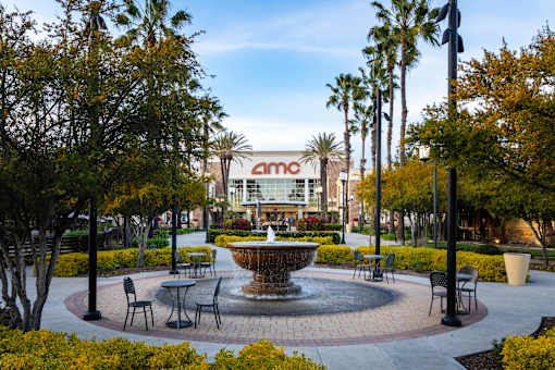 A fountain in the middle of a plaza with chairs and tables around it.