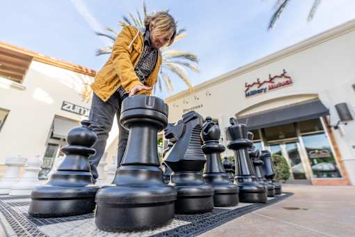 A person is playing with giant chess pieces outside a building.