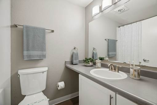A white toilet is in a bathroom with a white sink and a mirror.