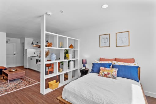 a bedroom with white walls and a white bed with blue and orange pillows