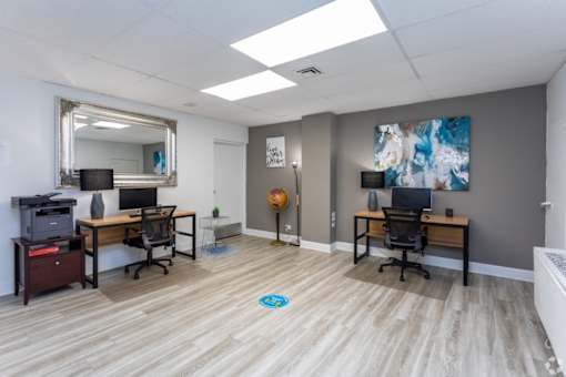 A room with two desks and a printer on a cabinet.